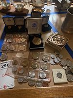Image of coin collection spread on table including the Kennedy half dollar necklace, loose and sleeved coins, and Polish medallions.