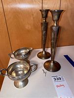 Two sterling silver candle stick holders, tall and tapered with flared tops and broad bases, shown on a wooden surface.
