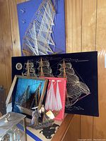 Group photo showing multiple vintage string art ships displayed on wooden panel, some with velvet backgrounds in blue, black, and red.