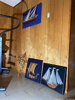 View showing three string art designs leaning against wood paneled wall: Viking ship, sail ship, and bird cage