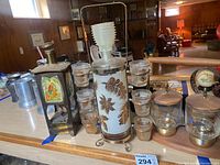 Overall view of vintage barware items on counter with decanter central, shot glasses around, wooden and glass beverage holder, and music box to the left.