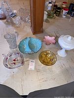 Overview photo of the lot showing various vintage ceramic and glass candy dishes, bowls, and a clear pressed glass pitcher on a table.