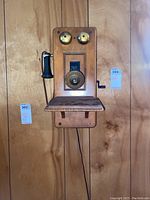 Full view of the vintage wood wall phone mounted on wood paneling, showing the face with handset and shelf.