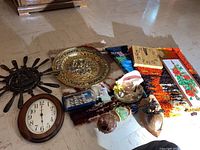Group of clocks, ship in bottle, metal wall art, brass plate, Hawaiian art, and colorful carpet square on the floor.