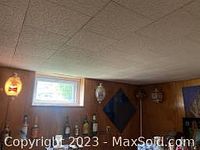 Three wall-mounted bar lights installed on wood-paneled wall under a window: Budweiser oval light, Country Club malt liquor light and carved coconut lamp