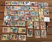 Top down view of 40 assorted 1966 Batman OPC Canada trading cards arranged in rows on a wooden table.