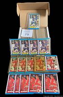 Photo showing a cardboard box full of O-Pee-Chee hockey cards with loose cards displayed in front: 4 Brett Hull cards, 5 Theoren Fleury rookie cards, 5 Joe Nieuwendyk second year cards, all in protective sleeves.