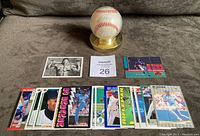 Photo showing an official American League baseball in a clear plastic holder with a gold-colored base, surrounded by 25 baseball cards laid out in front including colorful 'BO' Score card from 1990.