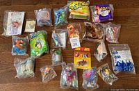 Top view of all 21 sealed fast food toys laid out on a floor showing various toys in plastic sealed packaging representing multiple pop culture franchises.