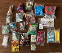Top-down view of 23 assorted sealed fast food toys spread on wooden floor, showing variety of characters and packaging styles.