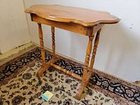 Side angle view showing scalloped edges and turned legs of the pine wood accent table on patterned carpet.