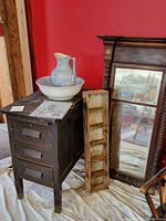 Photo showing vintage office side chest, ceramic bowl and pitcher on top, rustic wooden shelf leaning against side, and antique mirror reflected in background.