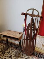 Photo showing antique children's school desk beside vintage wooden sled with sleigh bells hanging from the leather strap attached to sled.