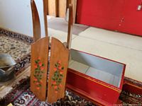 Photo of natural wood sled showing hand-painted floral decorative elements on the upright seatback, with curved wooden runners visible.