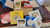 Boxes of collector's plates including Hummel and Schmid brands with clear lettering and illustrations on the boxes, arranged on a carpeted floor.