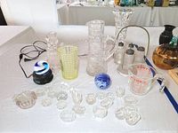 Overview of lot showing most glassware items including salt dips, vases, measuring cup, paperweight, and spoons