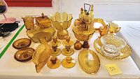 Photo showing entire group of amber depression glass items on a table, including bowls, candle holders, candy dishes, a pitcher, apothecary bottles, and a cruet set.