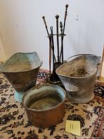 Overall view of fireplace tools, two ash buckets, and copper pan on a patterned rug.
