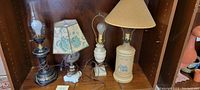 Four vintage lamps placed against a wooden backdrop on a shelf.