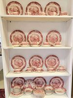 Shelves displaying red transferware plates, teacups, saucers and bowls from English Meakin with architectural and pastoral scenic patterns.