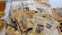 Stack of vintage historical newspapers from the mid 20th century, showing visible wear, yellowing, and prominent headlines referencing John F. Kennedy, WWII Allied invasions, and environmental disaster reports.