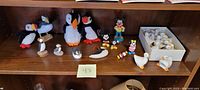 Shelf with puffin collectibles including wooden and plush figures, small Mickey and Minnie Mouse figurines, and ceramic duck napkin holders.