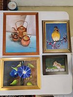 Four framed paintings placed on a white surface: still life of teapots, yellow bird on branch, blue morning glories, chipmunk eating nut.