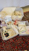Overview of four plastic bins filled with vintage linens, doilies, handkerchiefs, rabbit doll, and porcelain frog pot placed on carpet