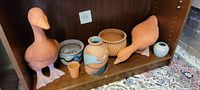 Front view showing both terracotta duck figures and assorted pottery planters on shelf