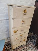 Frontal view of vintage painted pine chest of drawers showing five drawers with round wooden knobs and floral decal remnants.