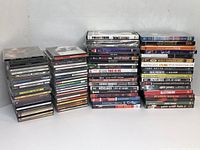 Photo showing multiple stacked CDs with artist names, displaying their titles and condition.