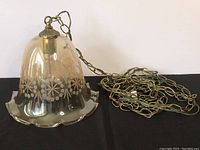 Full view of the scalloped bell-shaped etched glass hanging light fixture with chain laid next to it.