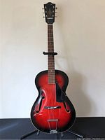 Full front view of red sunburst guitar on stand against neutral background