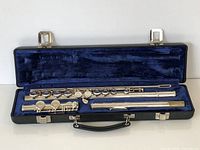 Full view of the three-piece Gemeinhardt flute laid in its open hard black case lined with blue velvet.