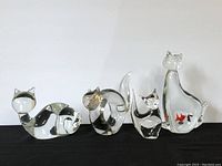 Front view of four clear glass cat figurines of different sizes displayed in a row on a black surface.