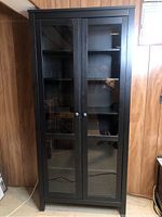 Front view of black Hemnes cabinet with glass panel doors in a basement setting.
