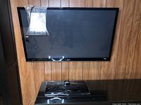 Front view of LG 50" plasma TV mounted on wood panel wall with remote control and table base mount on stand below.