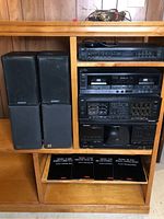 Four speakers stacked next to the shelving unit holding the stereo components and four original NEC manuals inside the shelf.