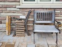Outdoor chairs positioned against stone wall; one fully assembled with wood slats and metal frame, the other disassembled with all parts accounted for including wood panels and metal side frames.