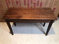 Full view of rectangular wooden piano bench with four legs on a tiled floor.
