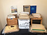 Wide view of the sheet music lot showing wooden crates, a box, and loose sheet music.