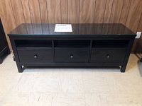 Full front view of black Hemnes TV unit with glass top and storage drawers beneath three open shelves.