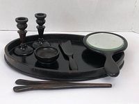 Photo showing the vanity set items arranged: two ebony candlestick holders, one larger and one smaller; oval ebony tray; hand mirror with ebony handle; small round dish; ebony shoe horn; and hair clip. Items show natural wood grain and vintage wear.