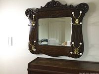 Front view of vintage wooden framed beveled mirror with four brass and white ceramic hooks attached at corners