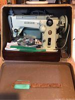 Singer 319K sewing machine inside open tan carrying case showing machine mounted on wooden base with green seam gauge on lid and accessories bag.
