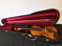 Open hard travel case with violin and bow inside, showing red velvet lining and black exterior.