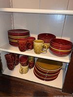 Red and mustard colored plates, bowls and mugs arranged on shelves showing quantity and color pattern