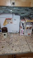 Image showing Welbilt bread machine, Moulinex coffee and spice mill, boxed Presto Salad Shooter, and boxed Wilton Dessert Decorator items.