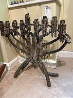 Full view of bronze menorah sculpture showing overall design, three-legged base, and nine candle holders with thick textured bronze forming a brutalist style.