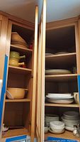 Wooden kitchen cabinet with shelves holding various dishware: white plates and bowls, glass serving bowls and plates.